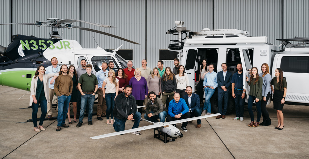 A group of people standing in front of a helicopter and a truck